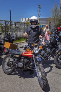 Participant élégant en costume trois pièces — et tant d'autres tenues tout aussi distinguées — au guidon de leurs motos respectives, unis avant le départ de la DGR Montréal 2026.
