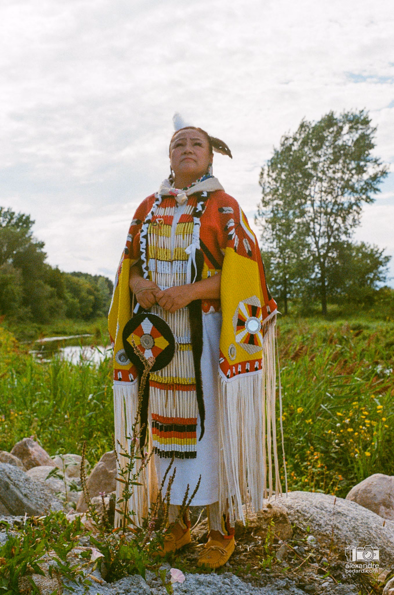 Portrait en photographie argentique d'une femme participante arborant une regalia traditionnelle richement ornée de perles et de rubans
