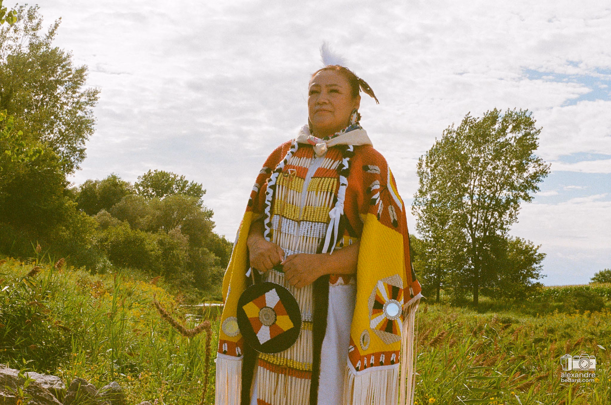 Portrait en photographie argentique d'une femme participante arborant une regalia traditionnelle richement ornée de perles et de rubans
