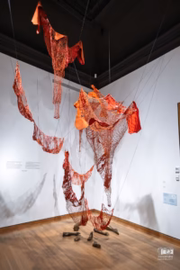 Objets du quotidien suspendus dans un maillage complexe de fils lors de l'exposition de Chiharu Shiota.