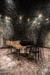 Piano calciné et chaises brûlées enveloppés dans une toile complexe de fils noirs suspendus au Musée des beaux-arts de Montréal.
